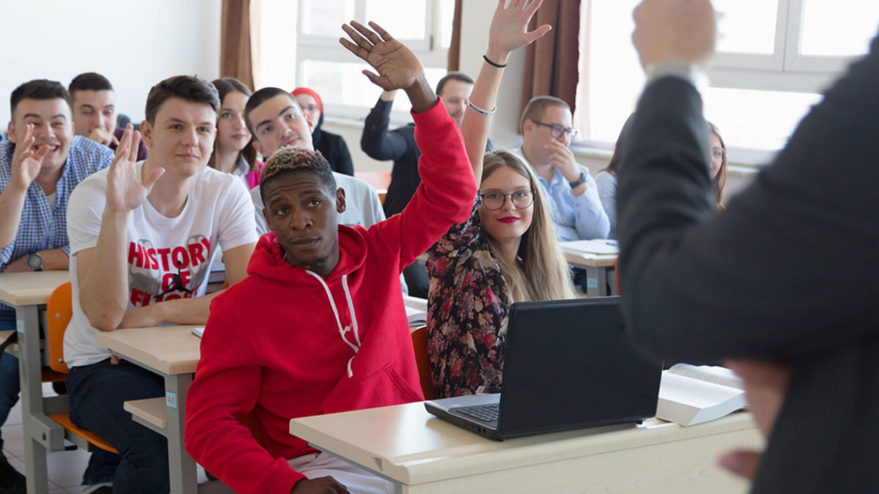 Students in classroom with hands raised to answer professor's question