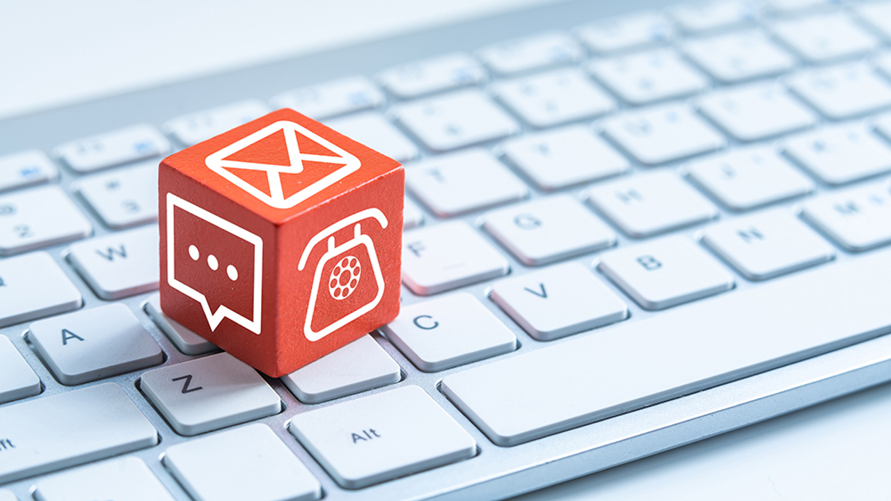 Red cube on a computer keyboard with a phone, email, and text bubble on it.