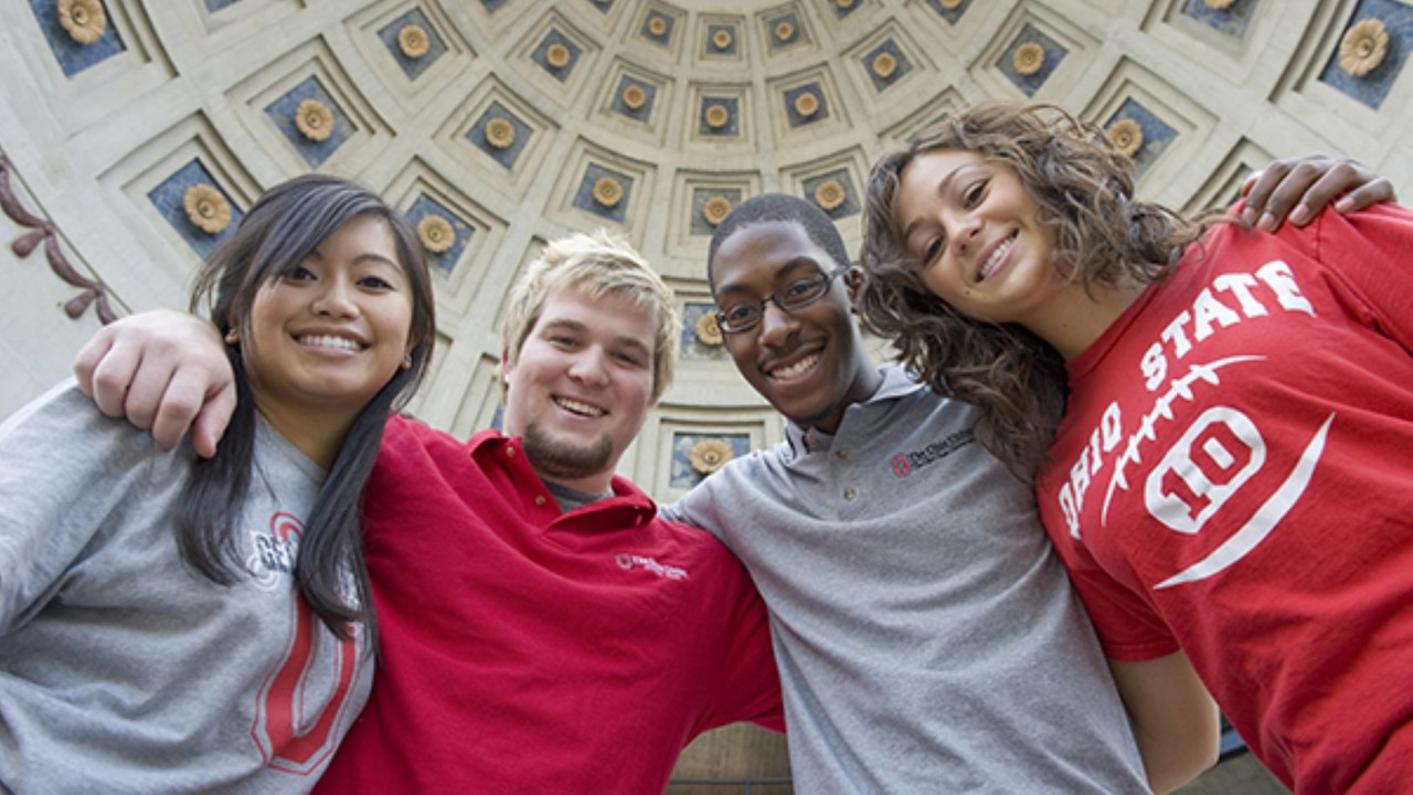 Four Buckeye students with their arms around their shoulders in front of Ohio Stadium