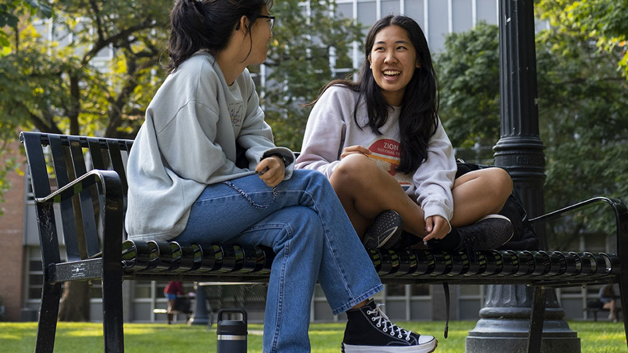 two women sitting on a bench outside and laughing.